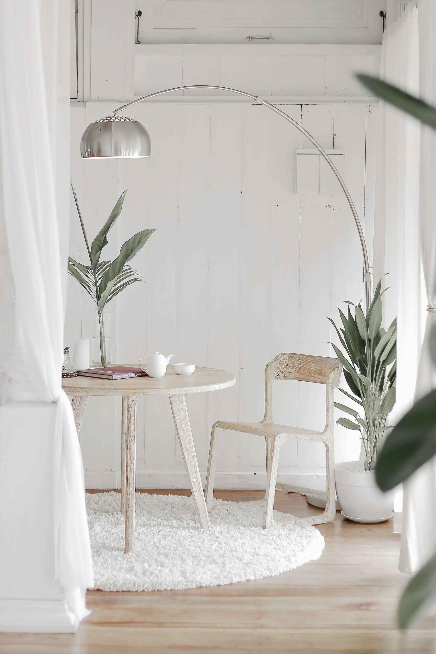 small table and chair next to a large floor lamp and plants