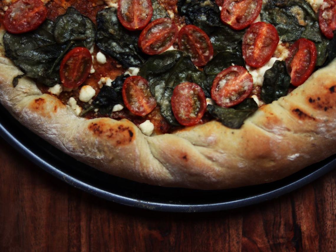close up image of a homemade pizza on a pizza pan on top of a wooden cutting board