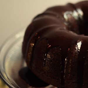 dairy free chocolate ganache on a chocolate bundt cake sitting on a glass cake stand