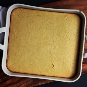 overhead view of honey cornbread in a white baking dish sitting on a wooden cutting board