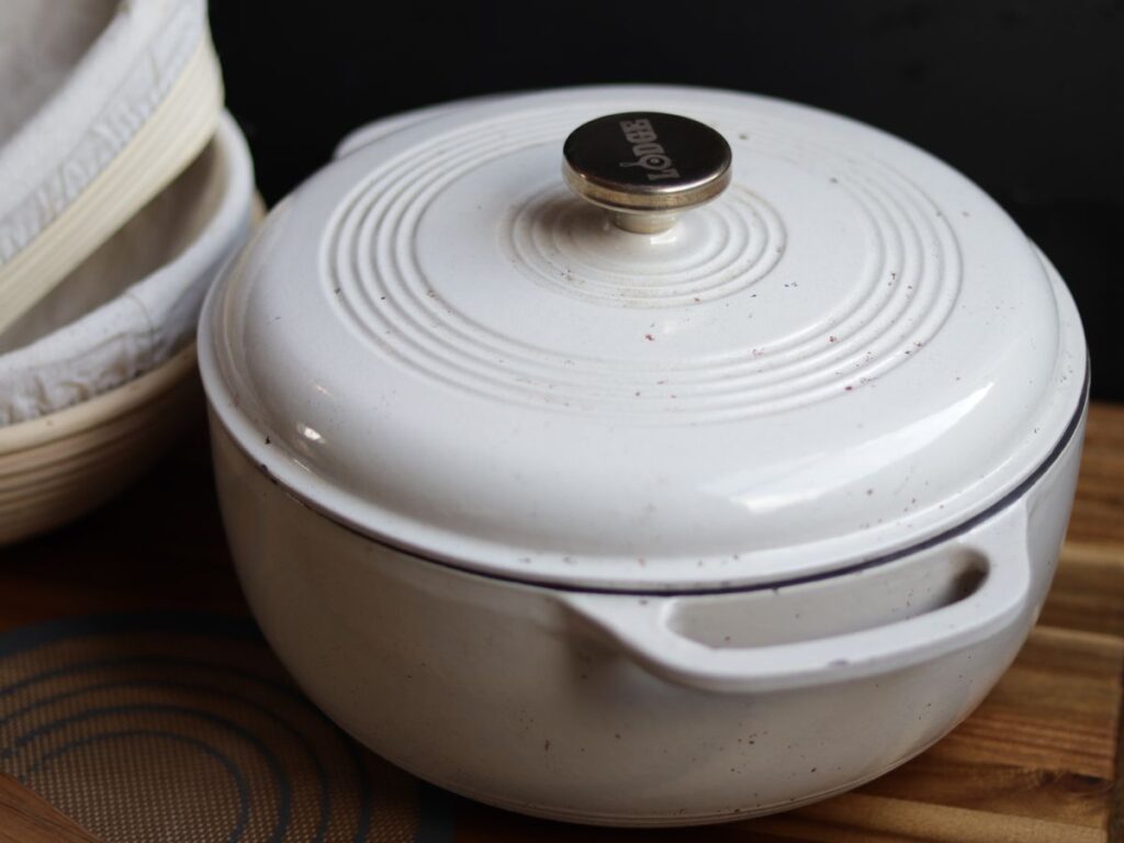 a dutch oven sitting on a wooden cutting board with sourdough bread supplies