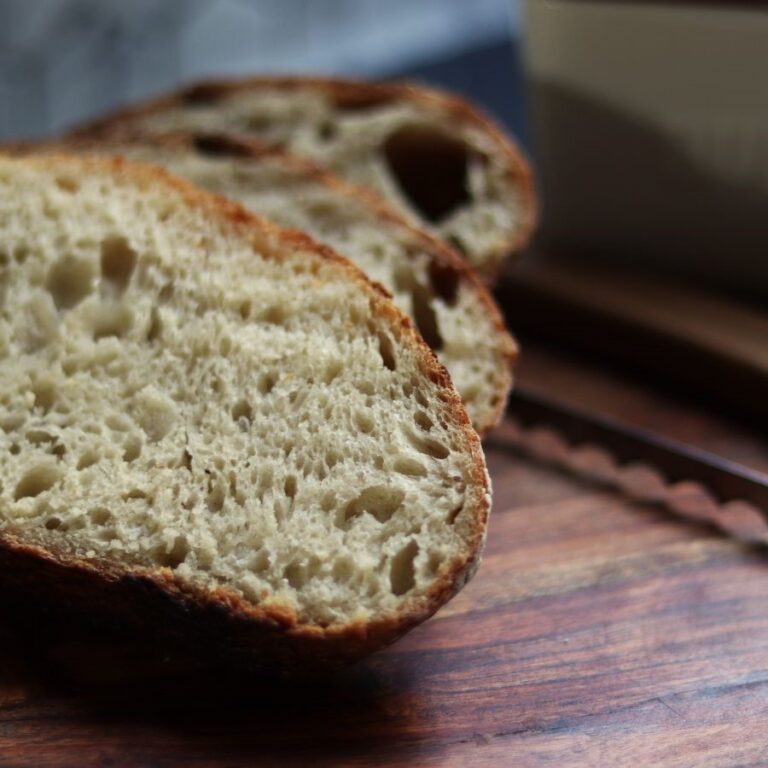 up close image of slices of sourdough bread on a wooden cutting board next to a bread knife and butter dish