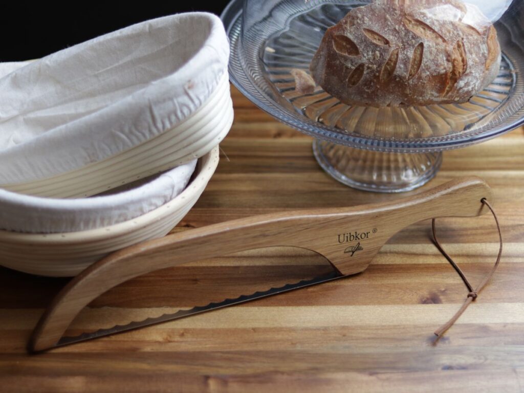 bread proofing banneton baskets with a bread knife and glass cake stand with a loaf of sourdough bread on top of a wooden cutting board