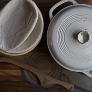 overhead image of a cast iron dutch oven, banneton baskets, a silicone baking sling and a bread knife