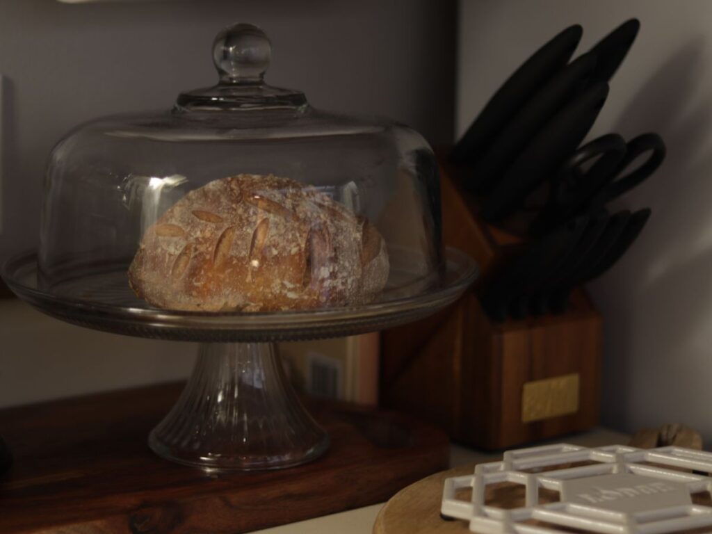 class cake stand on a wooden cutting board next to a knife block on a kitchen counter
