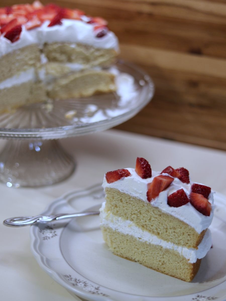 a slice of homemade vanilla cake with homemade whipped cream and strawberries on a small plate with fork