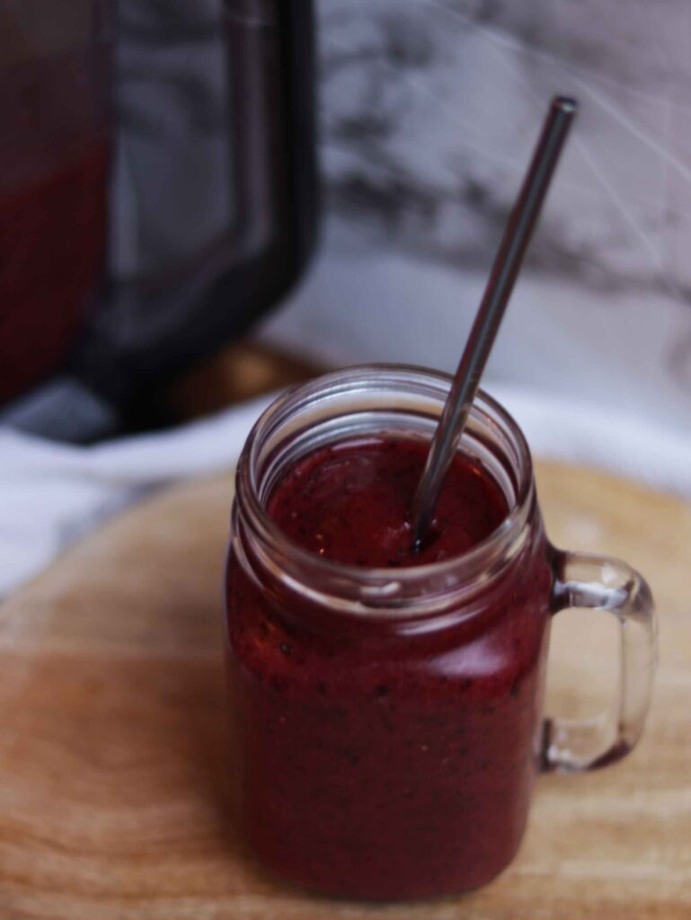 frozen fruit smoothie in a glass cup with a stainless steel straw